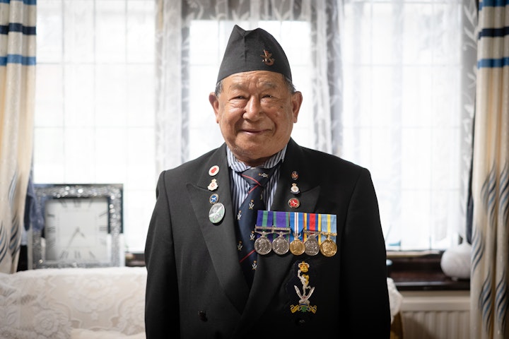 Open Britain: Portrait of a Diverse Nation - Til Man Rai was born in 1947 in the extremely remote village Deusa in Solukhumbu region, Mount Everest, Nepal. He was only 14 when scouts came to his village and brought him to the nearest city to join the Gurkha Boys Company. It took him one week to walk there. There, he was trained until aged 18. He then became a Radio Relay Operator for the Queen’s Gurkha Signals as soldier no. 2115429. He formally entered one of the world’s most elite fighting forces.
The Gurkhas are a unique organisation of soldiers from Nepal that have been fighting for Britain for over 200 years and still serve today. After the Anglo-Nepalese War of 1814-1816, Britain decided to recruit Nepali soldiers rather than fight them. These soldiers went on to fight major battles for the British and win 13 Victoria Crosses. In the World Wars, over 50,000 Gurkhas were killed, wounded or missing and nearly 5000 gallantry medals awarded.
Til Man served in what was then known as Malaya to support British troops in the jungle warfare of the 1962-1966 Borneo Confrontation. He was posted across army bases from Hong Kong to Singapore and Borneo. Til Man was made redundant before the 15-year requisite to get a pension.
Til Man returned to farming, basket weaving and carving to support his family in Deusa. But this became harder and harder. Selling his land to pay his way to the UK, he arrived in London in 2013 with the hope of finding means to support his wife and five children left behind in Nepal. He was 66 years old.
In the UK, Til Man didn’t know anyone except a fellow villager from Nepal who picked him up at the airport. They decided to take him into their home as he had nowhere to stay (See Pic). The little he is able to save from his benefits, he sends back home. He is now 76 and this is his only way to support for his family.
There are many isolated, impoverished elderly Gurkha veterans like him in the UK and Nepal. Many were forcibly made redundant before they could qualify for pensions. Those eligible for pensions only get a fraction of their British and Commonwealth counterparts. Historically their pension pay differences have been nearly 1000%.
Til Man Rai is hopeful despite missing his wife, kids and grandkids. He and his fellow Gurkhas continue to fight for their rights.