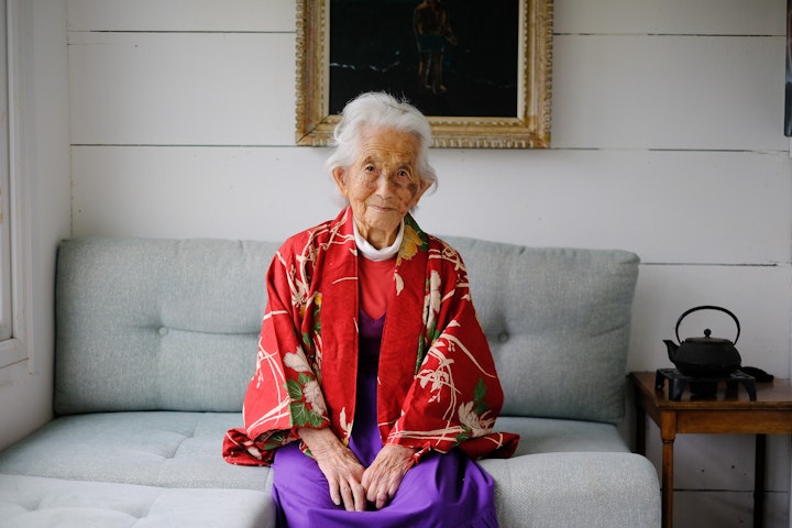 Open Britain: Portrait of a Diverse Nation - Michiko Mitsuishi Dodd, 101, was born in the seaside town of Kobe, Japan. One of 4, her eldest sister ‘eloped with an idiot’, breaking her father’s heart. He died when Michi was 12.
She met her husband Jeremy in 1947 at a party on an RAF base where he was serving in the hospital and she was working as an interpreter. “He looked very miserable and I felt sorry for him”. They had 3 sons and a daughter together. Jeremy came back to England leaving Michi to carry on alone in Japan. Life was hard at that time in Japan as single mothers were shunned by society. Her father-in-law arranged for them to get to England where they married.
After periods in the USA and Japan, they returned to the UK and soon after divorced. Michi and the children moved into a railway carriage along the south coast with money given to her by her father-in law. Michi remembers haggling hard to get the price down from £3000 to £2750. It was very basic to start with, with no running water, gas etc., but luckily Michi was ‘handy’ and learnt many building skills to make it ‘home’.
She still lives in the converted carriages 60 years later, currently being cared for by her daughter Rachel. Michi’s hearing has all but gone, which made this process both challenging and charming in equal measure.
Michi still happily drove herself around until recently stopped by the police on her way to hospital. She refused to get out of the car, so they followed her, eventually impounding the car and her license. Michi was furious.