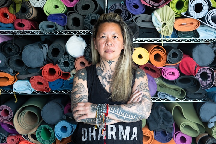 Open Britain: Portrait of a Diverse Nation - “Life, like those yoga mats, can be messy. It’s how we allow them to unravel and unfold that enables us to make sense of the mess instead of sanitising our experience.” Cat Alip-Douglas.
Cat Alip-Douglas was born in Manila, Philippines in 1972. She moved to New York with her family at the age of seven. Cat speaks with a subtle soft East Coast accent.
Her life in metropolitan Manila was a privileged one. At the time it was still under a dictatorship and divided into the haves and have-nots. Her parents employed domestic help not out of desire or necessity but to aid those in need. She remembers the first morning of school in the US being laughed at by her sisters for sitting on the end of her bed with arms raised waiting to be dressed. However, she took to independence quickly. She loved being a ‘latch-key kid’ in unruly 80’s NY.
At Rutgers University she discovered the NYC rave scene. Fast Forward from all night partying to planning parties at Condè Nast, ‘definitely no place like it at that time’. Cat loved her job but worked ridiculous hours and discovered yoga to help with the stress and insomnia.
September 11th 2001, Cat was in the office when flight 11 crashed into the North Tower. The focus on an upcoming work event meant she remained rooted to her desk, highlighting her ‘obliviousness and self-absorption’. Like for so many this turned out to be a wake-up call and a defining moment in her life. The yoga practice and its spiritual learnings became a lifeline.
In 2004, her London based tattoo artist boyfriend encouraged her to pack in the rat race and move to London. It took a while to adapt to the ‘slower’ pace of London, but turns out, it was exactly what she needed. Yoga took over. When Cat and her husband, who she met through her tattooist-ex, inherited the London Jivamukti Centre in 2011 it evolved into their own Sangyé Yoga School (Sangyé is Tibetan for Buddha - awakened
The change to Sangyé couldn’t have been smoother, thanks to the incredible commitment of students and teachers, but Covid, unsurprisingly, hit hard: they’re still nowhere near pre-pandemic levels. However, unlike many centres, they’re still standing and providing a valuable service to the North-West London community.