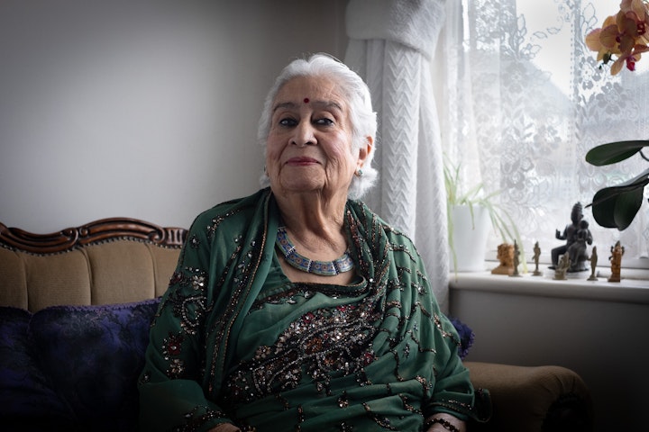 Open Britain: Portrait of a Diverse Nation - Dr Jai Kumari Gir was born in 1934 in Hydrabad, a childhood she describes as ‘completely idyllic’. In a sign of things to come she delivered two of her own brothers when her mother went into labour. They called her the ‘gypsy girl’ because of her incessant lust for travel and adventure and it soon became clear she wanted to make a career for herself in England. Not least because she had a thing about a classy English gentleman, with a particular penchant for Roger Moore.
She buckled down and studied hard. It took 4 months to get exams results in those days as the papers were shipped back to the UK. She gained a place at Girton College, Cambridge but because of currency restrictions couldn’t take it up. She continued to study in India till the restrictions eased and then took a place at West London School of medicine (now Charring Cross Hospital) in 1956.
She was quick to integrate into the UK something she believes was helped by the lightness of her skin. She ‘loved necking ciders’ in and around Holland Park and Notting Hill. As a Gynaecologist for many years and then a doctor in General Practice, she stresses the Health Service in the 1960’s was under the same pressure due the squeezing of resources.
Jai believes the way to stop any sort of discrimination is not through Governments or legislation, nor schools and their teachers, but with mothers themselves. She also says Britain is a country of immigrants. It always has been. ‘There are very few families who can claim to be entirely English in their bloodline’. No one, she says, ‘owns this Earth, and everything is on loan.’ Which means we should all be welcomed, wherever it is on the Earth, and ‘the British have been rather wonderful at this’.
I met her with her son Ayas, as I finished taking my snaps, he said with great fondness ‘You look so very wise’., ‘No I don’t I look like a witch.’