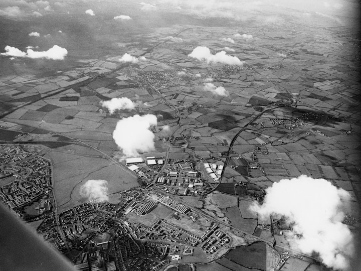 Aerial photograph showing the industrial areas of Yate with Badminton Road Trading  Estate, Stover Trading Estate and Beeches Industrial Estates in the centre of the image. 
The main Gloucester to Bristol railway line is seen running diagonally  from the bottom right to the centre of the left edge of the image with the above mentioned estates located just above (to the west) of the line. 
To the east of the line, running adjacent to the track is the site of Parnalls factory. A tree-less Westerleigh Common is also  adjacent to the same railway line but more to the south (left). Newman's Factory is in the bottom right of the photo next to the wing of the aircraft that took the photo and Westerleigh Road can be seen heading south from the factory along the eastern boundary of the Common. 
The main London to Swansea railway line running east to west can be seen on the left hand side of the image. 
The Thornbury Branch Lane can be seen snaking out of Yate Station to the west then north until exists the image on the middle right edge of the image.
Badminton Road (A432) can be seen heading west out of Yate passing through  Coalpit Heath to the upper middle centre of the image with Frampton Cotterell adjoined to its right (north).
The River Severn that  separate England and Wales can be seen to the west in the top right corner of the image which the main London line passes under via a tunnel.