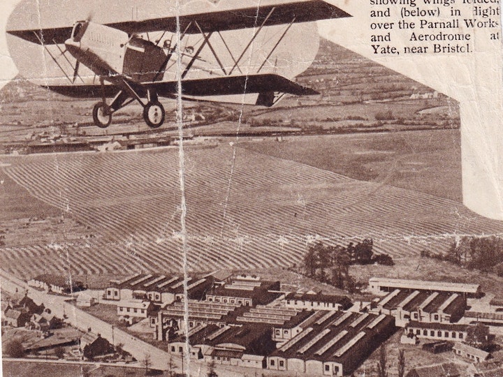 Photograph of a cutting of a magazine article illustrating the Parnall Elf aircraft over the Parnall Aerodrome at Yate with the Newman's engine factory in the foreground and the Parnall's factory in the background direcctly underneath the wheels the plane.