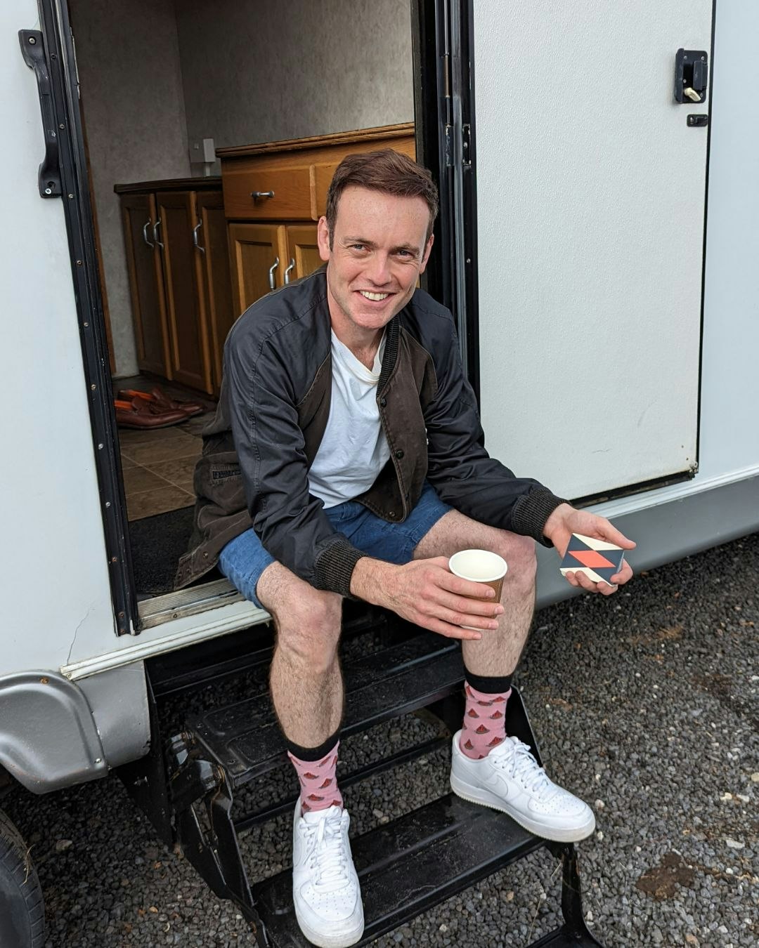 Brendan Patricks sitting on trailer steps with a coffee on a film set
