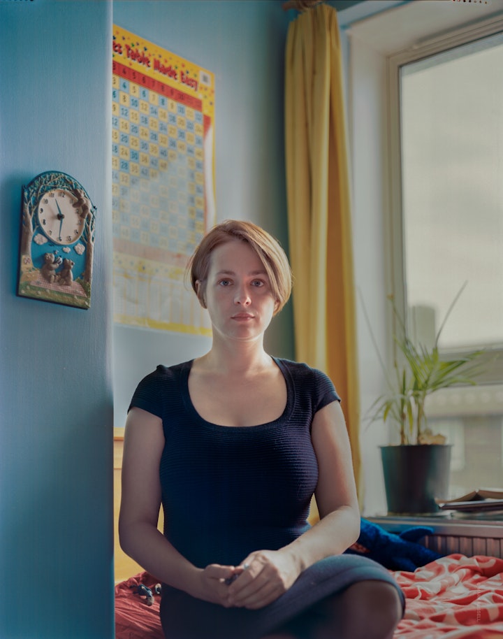 A portrait of Joanna sitting in her young son's brightly coloured bedroom with posters and a novelty clock on the wall.