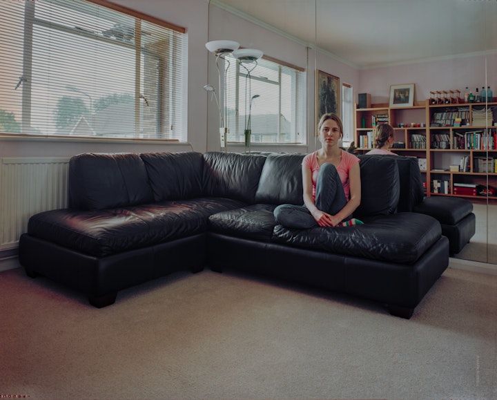 A portrait of Tatjana, sitting, knee-up on a wide leather sofa in her living room.