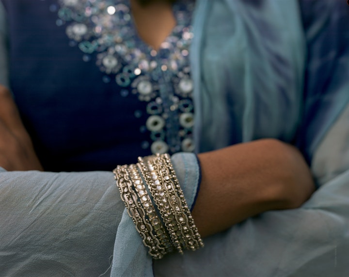 A close-crop portrait of Yasmin, whose arms are folded and are showing silver bangles over her decorated blue dress.