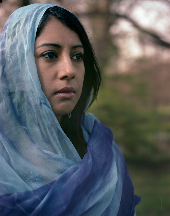 A head-and-shoulder portrait of Yasmin, looking off camera wearing a blue headscarf.
