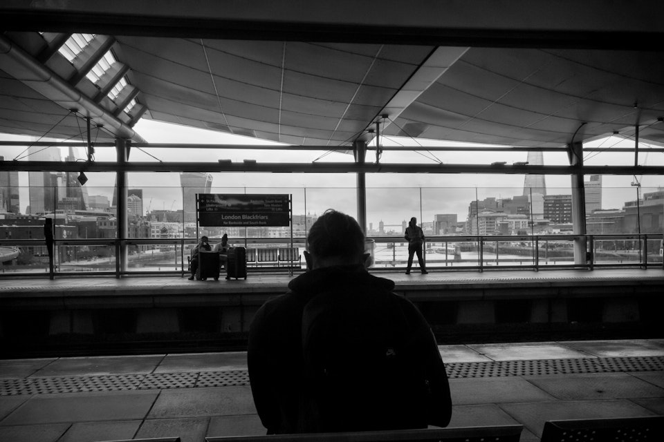Street Folio I - A man waits on the platform at Blackfriars station with the city of London, the Shard and Tower Bridge in the background.