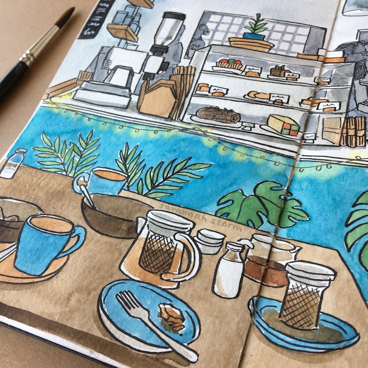 Sketchbooks - A sketchbook page of a coffee shop interior, a table filled with cups and the counter with cakes and coffee equipment in the background, illustrated using ink and watercolour paints.