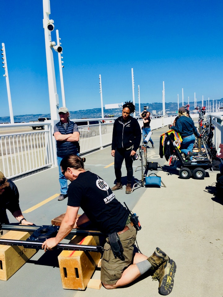 Key Grip Jason Noel (kneeling) and grip Alba Roland ready the dolly while location manager Jonathan Shedd watches for pedestrian bikers while working on the Bay Bridge.