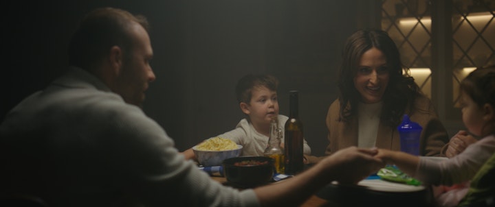 family sitting at living room table holding hands and praying dinner and food on table