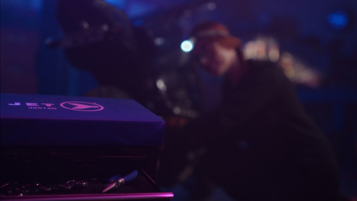 A woman fixing a motorcycle near a blue tool box, in a neon and dimly lit garage