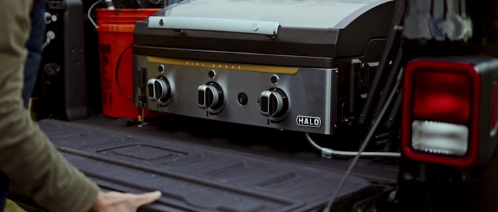 A man opening the back of a jeep with a grill on it, preparing for a cookout or camping trip.