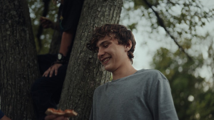 teenage boy with pizza standing by a tree with friends