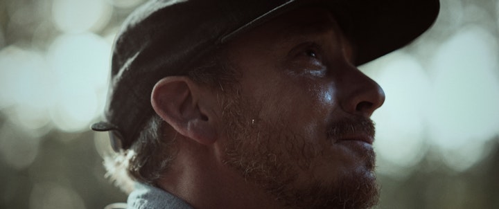 A man wearing a hat crying and smiling, gazing off into the distance.