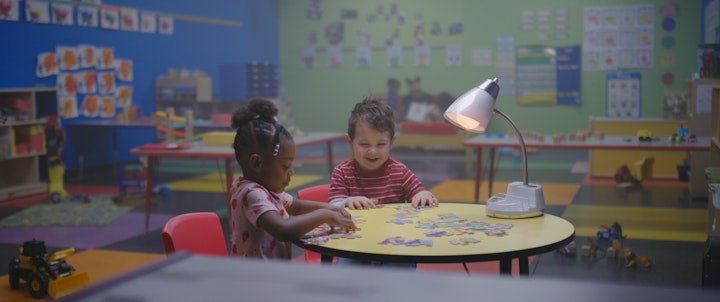 kids smiling and laughing at table in a classroom daycare building, playing with puzzle