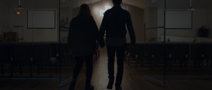 a silhouetted couple walking into a church holding hands, dimly lit