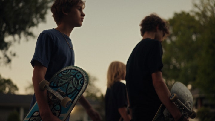 teenagers with skateboards walk down the street at sunset