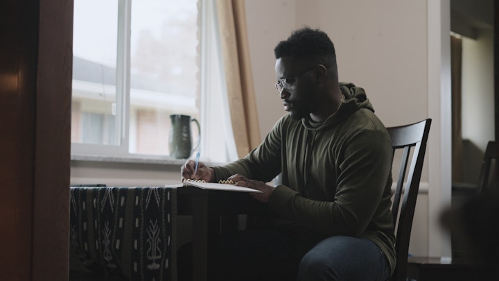 a man sitting at a kitchen table writing and taking notes looking sad thoughtful