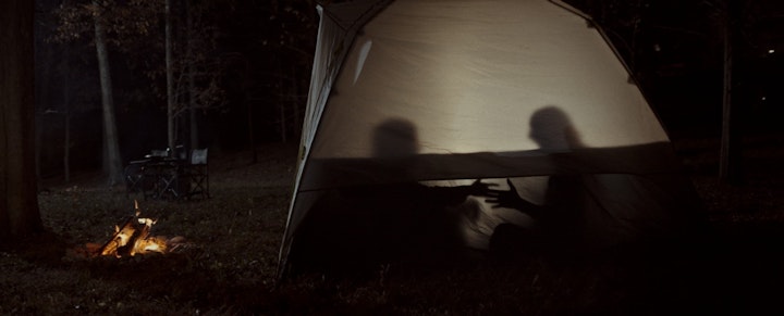 Two friends sitting in a tent under a starry night sky, enjoying each other's company and the peacefulness of nature.