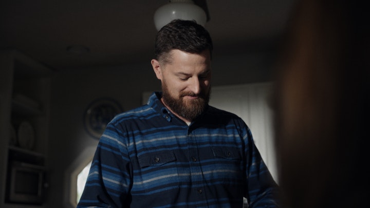 man in kitchen wearing blue flannel pours coffee for family makes breakfast