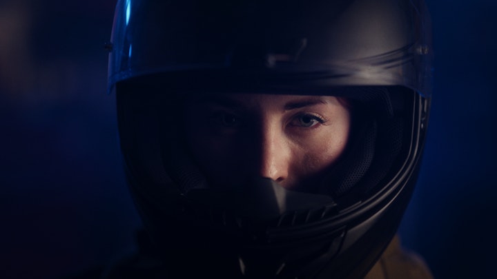 A woman in a helmet, riding a motorcycle, ready for action in a dimly lit room.