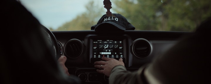 A person driving a car with a tablet on the dashboard, adjusting climate control