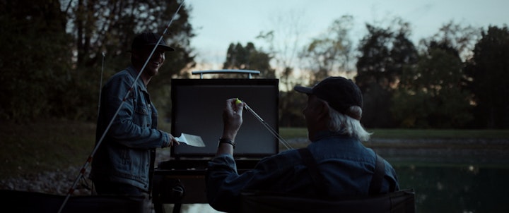 Two people peacefully seated next to a lake, fishing and cooking, enjoying a quiet evening