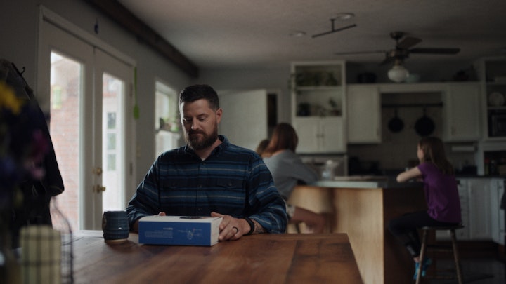father in living room table opening box and drinking coffee with kids in background