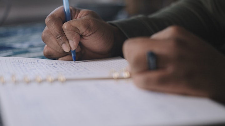close up of hands writing notes with pen in a notebook on paper
