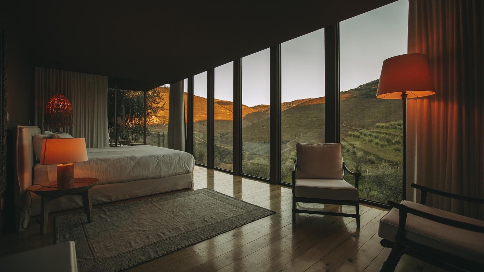 Luxury hotel suite overlooking the Douro Valley vineyards in Portugal at sunset, with floor-to-ceiling windows and panoramic countryside views.