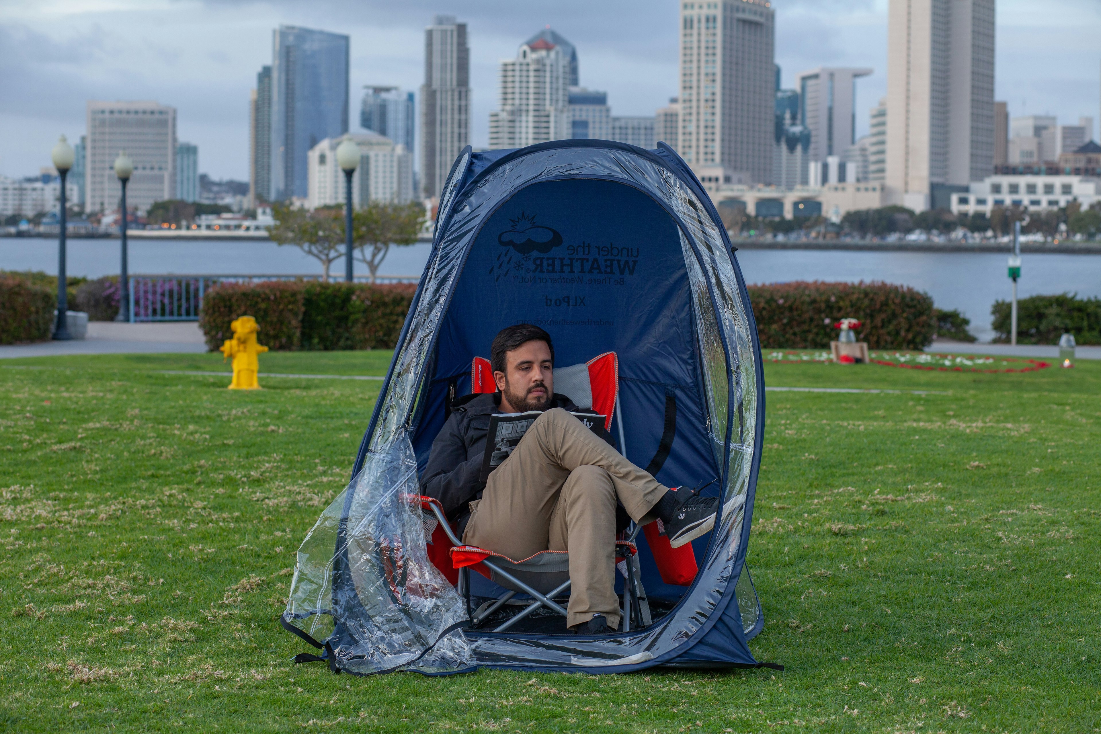Alexis Duran reading a book inside his chair pod in Coronado with the San Diego skyline behind him.